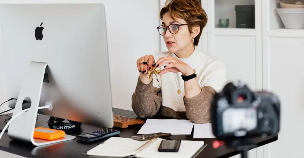 A professional woman engaged in a virtual meeting setup at her home desk, using a computer and camera.